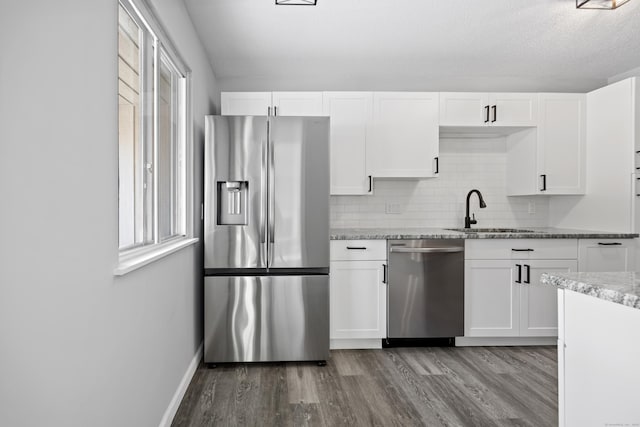 kitchen featuring light stone countertops, white cabinetry, stainless steel appliances, decorative backsplash, and sink