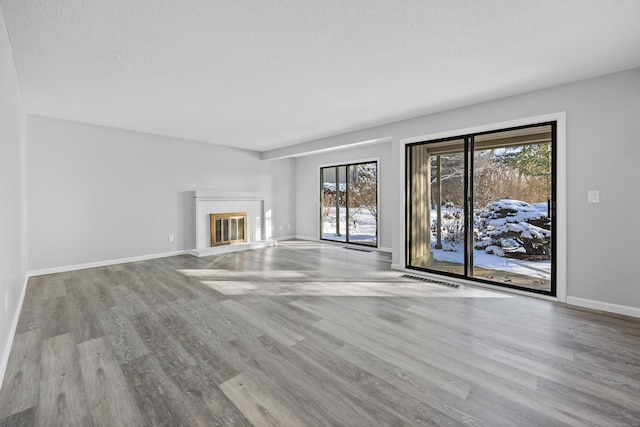 unfurnished living room featuring light hardwood / wood-style floors, a tile fireplace, plenty of natural light, and a textured ceiling