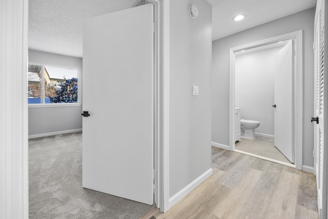 corridor with light wood-type flooring and a textured ceiling