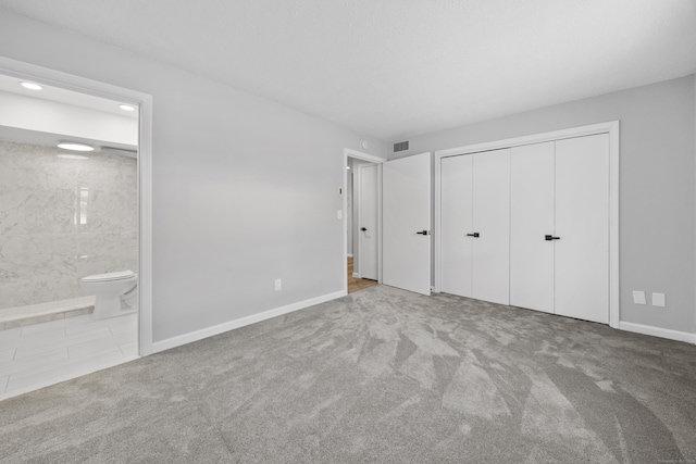 unfurnished bedroom with light carpet, a closet, and ensuite bathroom