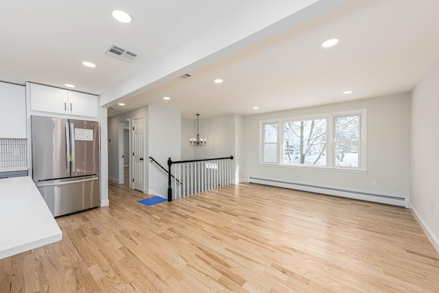 kitchen with hanging light fixtures, stainless steel refrigerator, baseboard heating, white cabinets, and light wood-type flooring