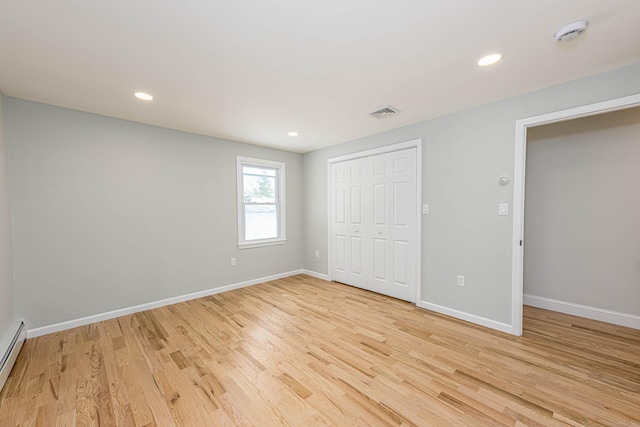 unfurnished bedroom with light wood-type flooring, a baseboard radiator, and a closet