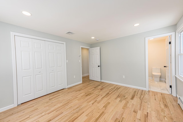 unfurnished bedroom featuring light hardwood / wood-style flooring, a closet, ensuite bath, and a baseboard heating unit