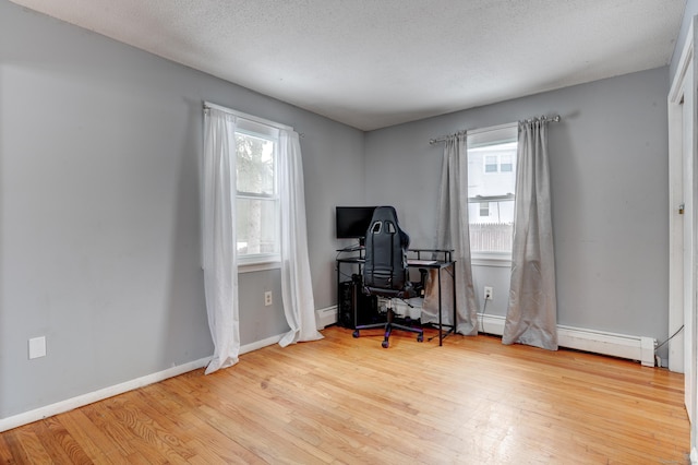 office space with a textured ceiling, a baseboard radiator, light hardwood / wood-style floors, and a healthy amount of sunlight