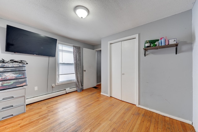 unfurnished bedroom with baseboard heating, a closet, light hardwood / wood-style floors, and a textured ceiling