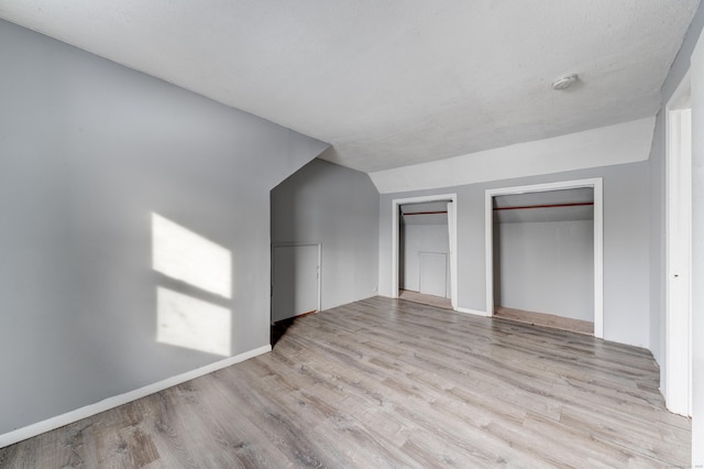 unfurnished bedroom with multiple closets, lofted ceiling, and light wood-type flooring