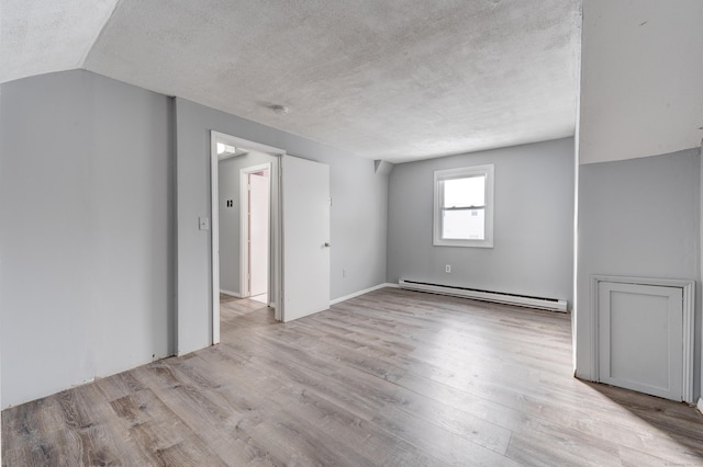 spare room featuring light wood-type flooring, vaulted ceiling, a textured ceiling, and baseboard heating