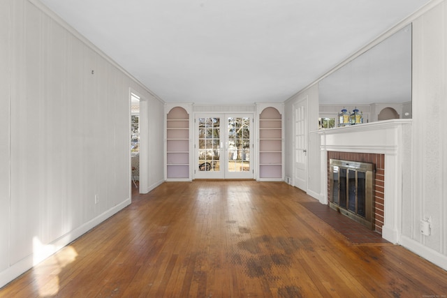 unfurnished living room with a brick fireplace, wood-type flooring, built in features, and ornamental molding