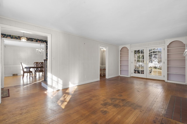 spare room featuring dark hardwood / wood-style flooring, built in shelves, and a chandelier