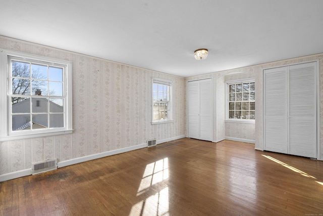 unfurnished bedroom with multiple windows, hardwood / wood-style flooring, and two closets