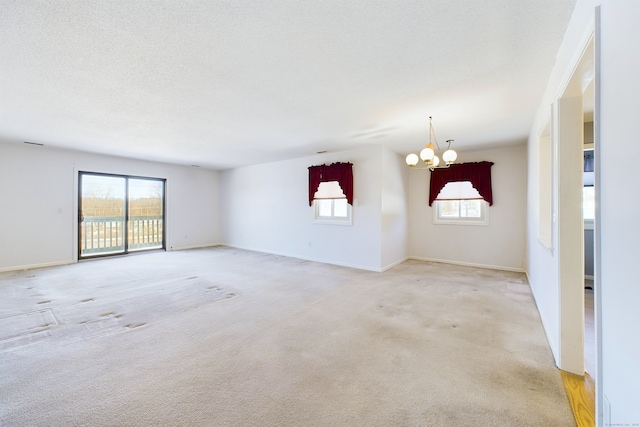 spare room featuring a textured ceiling, light carpet, a wealth of natural light, and a notable chandelier