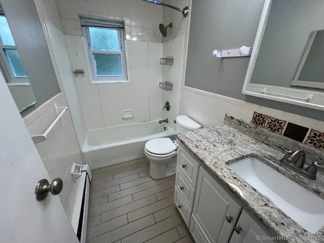 full bathroom with tile walls, vanity, tiled shower / bath, a baseboard radiator, and toilet