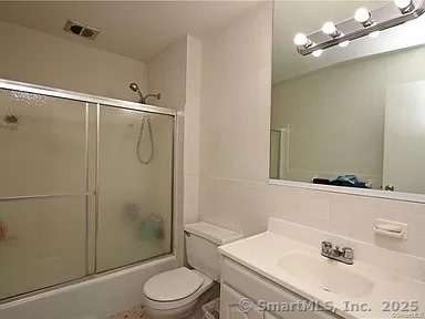 full bathroom with bath / shower combo with glass door, vanity, and toilet