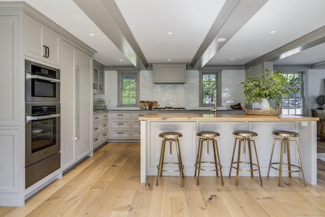 kitchen featuring gray cabinetry, tasteful backsplash, light hardwood / wood-style floors, and a breakfast bar area