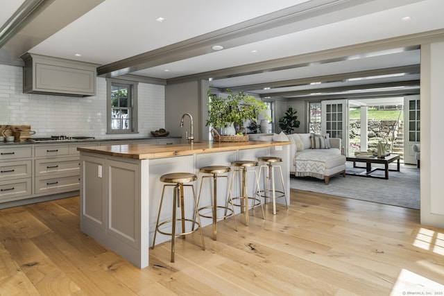 kitchen featuring gray cabinets, a kitchen island with sink, a kitchen breakfast bar, stainless steel gas stovetop, and light wood-type flooring