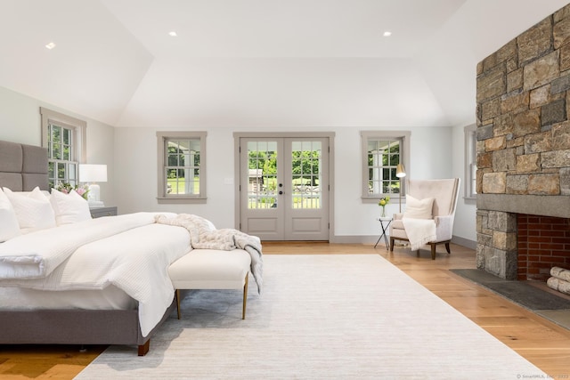 bedroom featuring lofted ceiling, access to outside, a stone fireplace, and light hardwood / wood-style floors