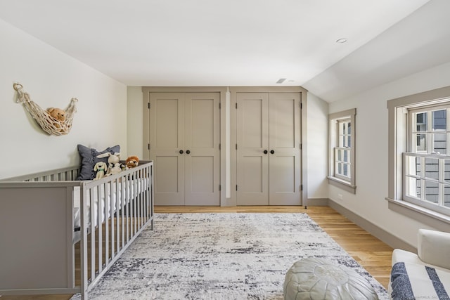 bedroom featuring lofted ceiling, light hardwood / wood-style flooring, and two closets