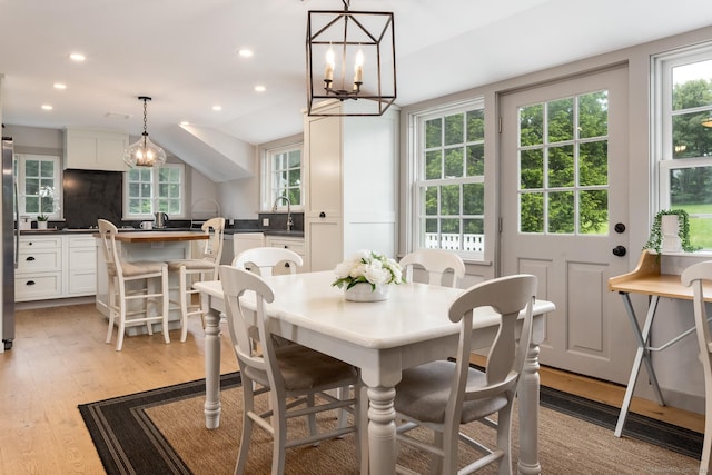 dining room featuring lofted ceiling, sink, and light wood-type flooring