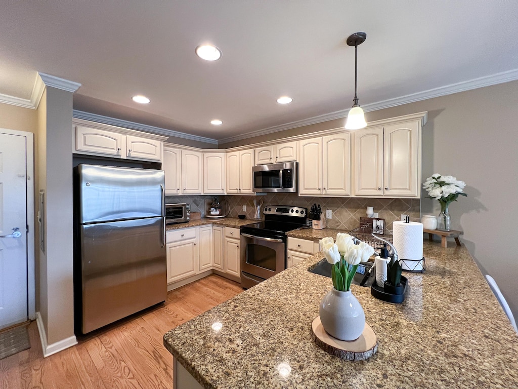 kitchen featuring crown molding, appliances with stainless steel finishes, decorative backsplash, light wood-type flooring, and decorative light fixtures