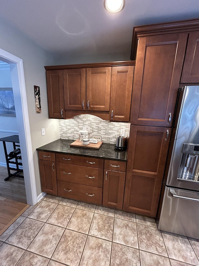 kitchen featuring light tile patterned flooring, backsplash, dark stone counters, and stainless steel fridge with ice dispenser