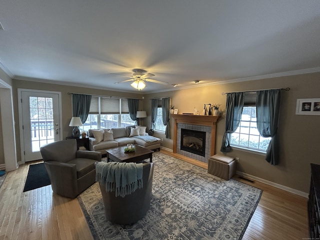 living room with a tiled fireplace, crown molding, a wealth of natural light, and light hardwood / wood-style floors