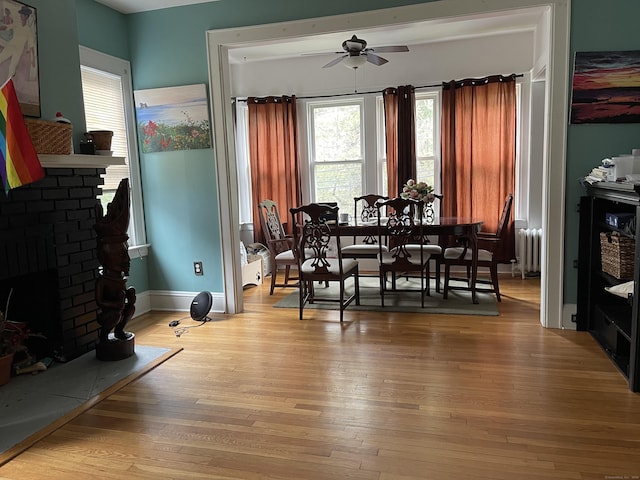 dining area with a brick fireplace, radiator heating unit, ceiling fan, and light wood-type flooring