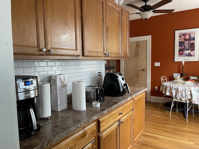 kitchen featuring ceiling fan, dark stone counters, light hardwood / wood-style flooring, and decorative backsplash