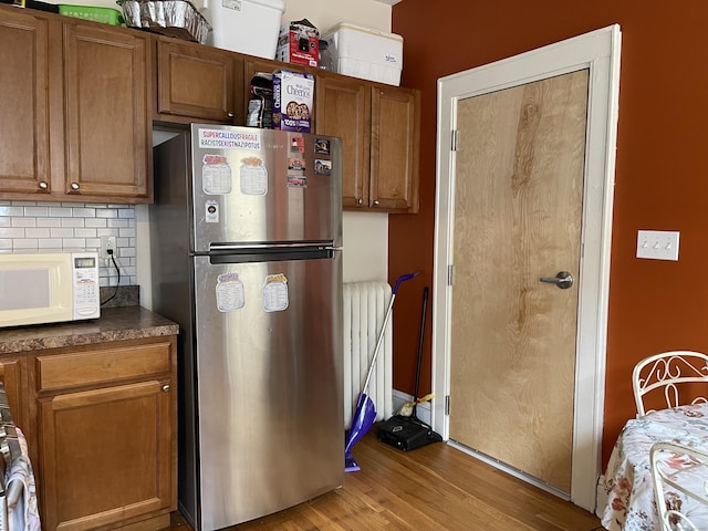 kitchen featuring radiator heating unit, light hardwood / wood-style floors, decorative backsplash, and stainless steel fridge