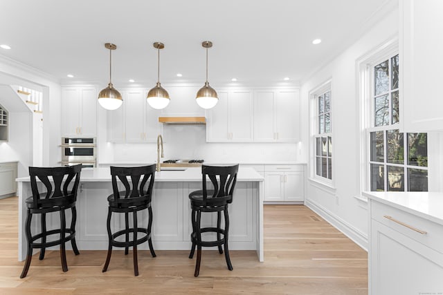 kitchen with pendant lighting, white cabinets, light wood-type flooring, a kitchen bar, and ornamental molding