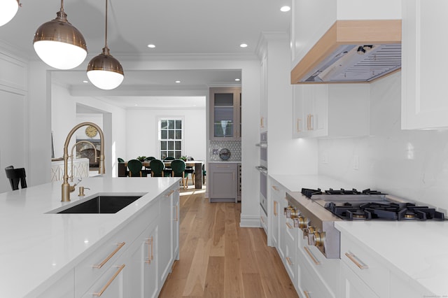 kitchen featuring stainless steel gas cooktop, custom range hood, hanging light fixtures, white cabinets, and light stone counters