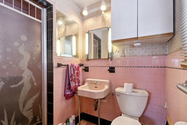 bathroom with sink, a shower with door, toilet, and tile walls