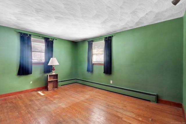 spare room with light hardwood / wood-style floors, baseboard heating, and a healthy amount of sunlight