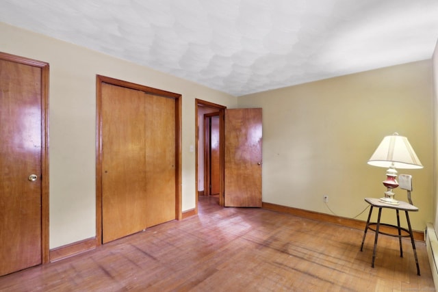 unfurnished bedroom featuring a closet, hardwood / wood-style flooring, and baseboard heating