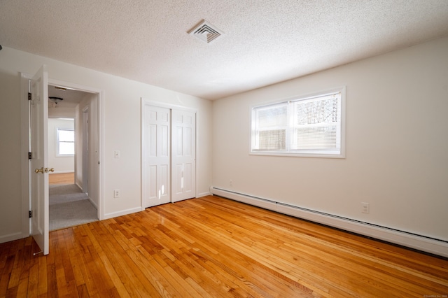 unfurnished bedroom featuring a baseboard heating unit, hardwood / wood-style floors, a closet, and a textured ceiling