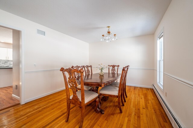 dining area with baseboard heating, light hardwood / wood-style floors, and a notable chandelier