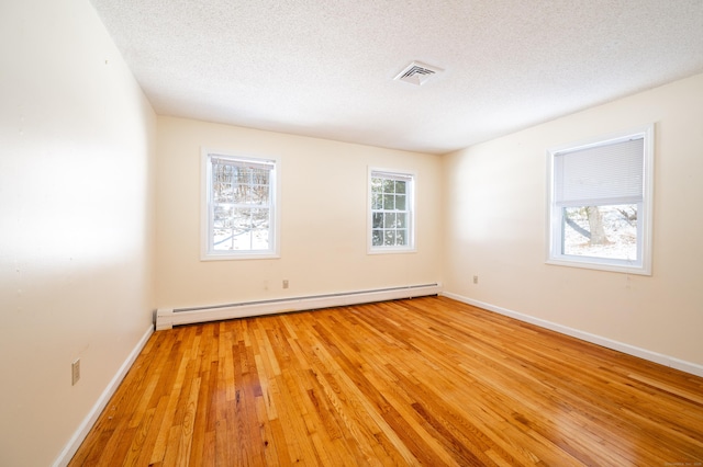 empty room featuring plenty of natural light, a baseboard heating unit, and a textured ceiling