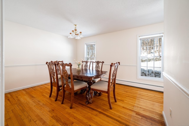 dining room featuring a notable chandelier, a wealth of natural light, light hardwood / wood-style floors, and a baseboard heating unit