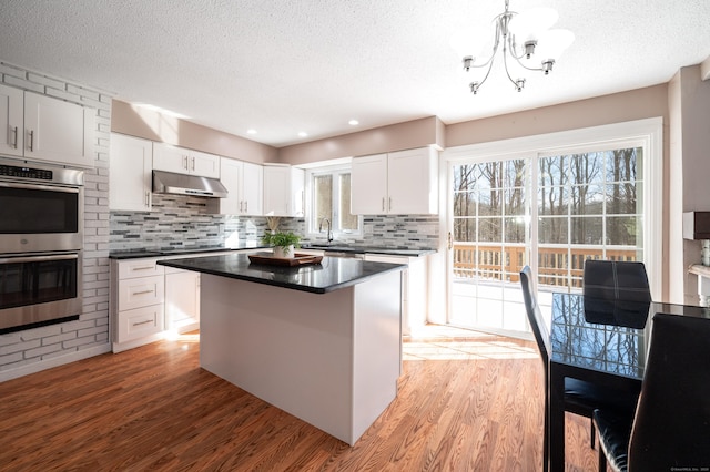 kitchen with sink, white cabinets, hanging light fixtures, a center island, and stainless steel double oven