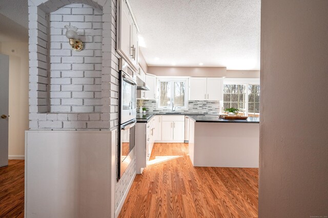 kitchen with sink, white cabinetry, light hardwood / wood-style floors, a textured ceiling, and decorative backsplash