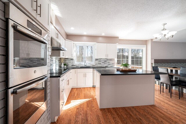 kitchen featuring white cabinetry, sink, stainless steel double oven, and decorative light fixtures