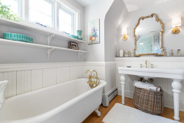 bathroom featuring wood-type flooring, a baseboard heating unit, and a tub to relax in