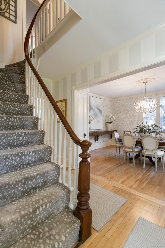 stairs featuring hardwood / wood-style flooring, crown molding, and a notable chandelier