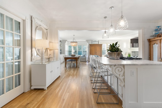 kitchen featuring hanging light fixtures, ornamental molding, white cabinets, and light hardwood / wood-style flooring