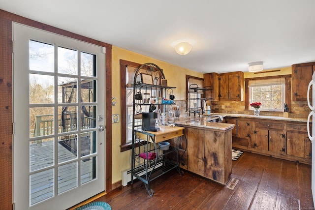 kitchen featuring baseboard heating, decorative backsplash, sink, dark hardwood / wood-style floors, and kitchen peninsula