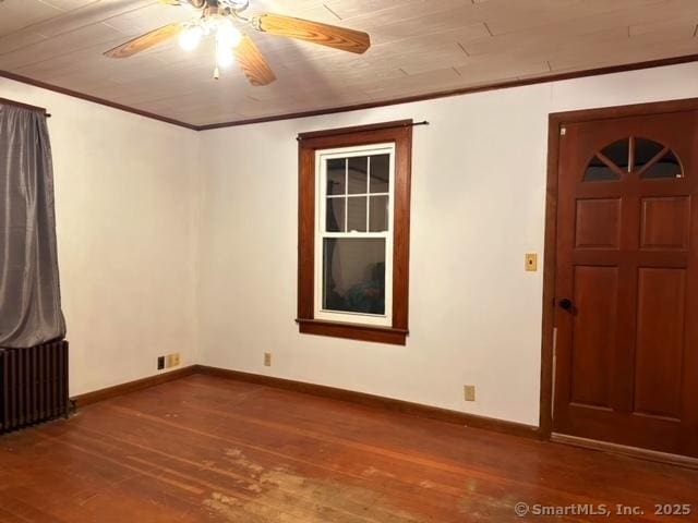 empty room with wood finished floors, baseboards, radiator heating unit, ceiling fan, and ornamental molding