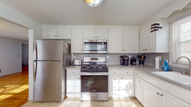 kitchen featuring appliances with stainless steel finishes, sink, white cabinets, a textured ceiling, and decorative backsplash