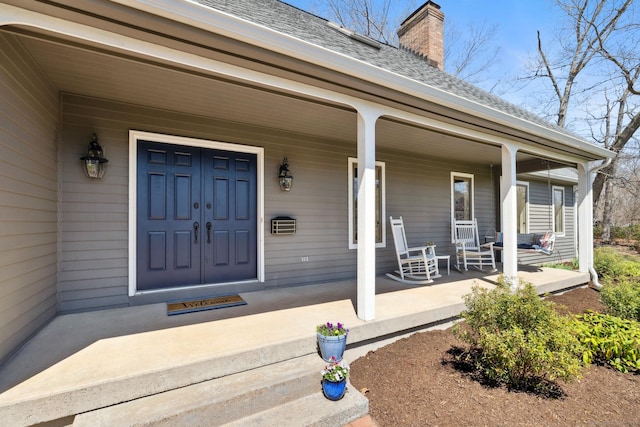 doorway to property featuring a shingled roof, a chimney, and covered porch
