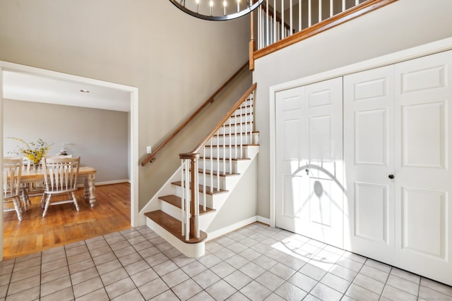foyer entrance with baseboards, a towering ceiling, stairs, and light tile patterned floors