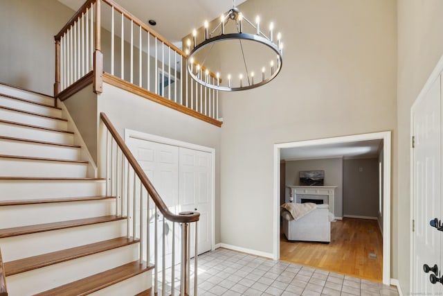 stairway featuring tile patterned floors, baseboards, an inviting chandelier, a high ceiling, and a fireplace