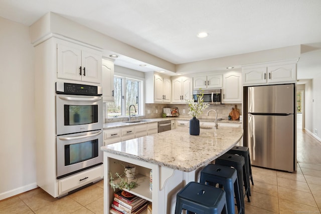 kitchen featuring a sink, decorative backsplash, white cabinetry, appliances with stainless steel finishes, and light stone countertops